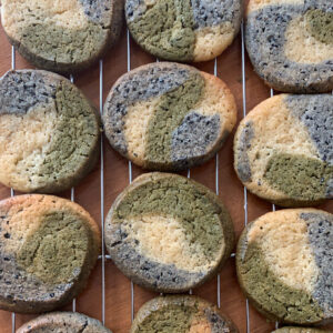 Photo of 12 cookies with a marble pattern of green (matcha), black sesame (black) and vanilla (white) on a baking rack.