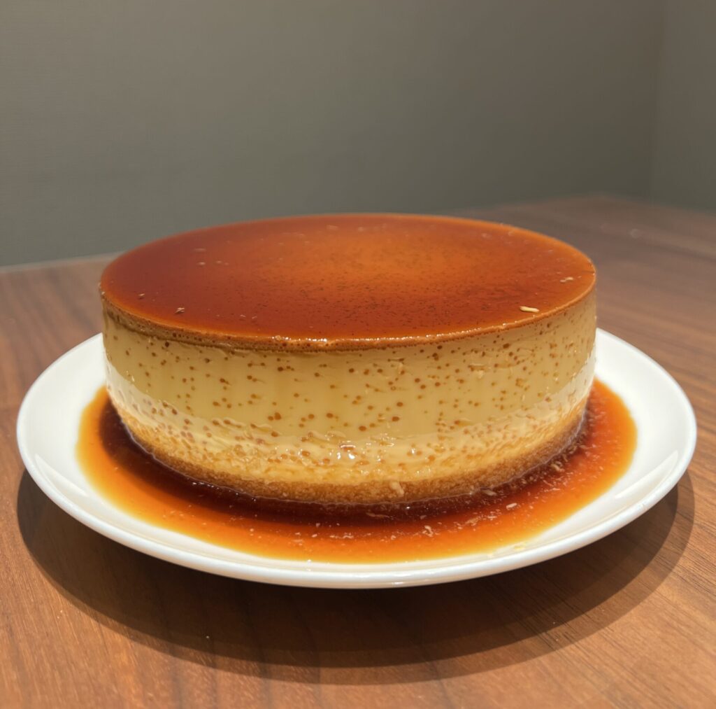 A Japanese purin cake that is similar to a leche flan on a plate with a pool of caramel on the bottom. The cake has 2 layers with a purin layer with a caramel sauce on top with a sponge cake layer on the bottom. 